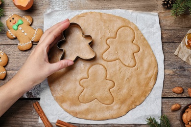 Photo of Woman making Christmas gingerbread man cookies at wooden table, top view