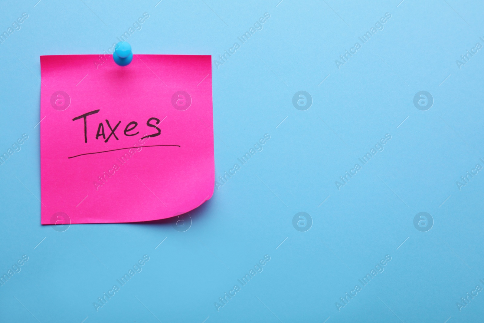 Photo of Paper note with word Taxes pinned on light blue background, space for text