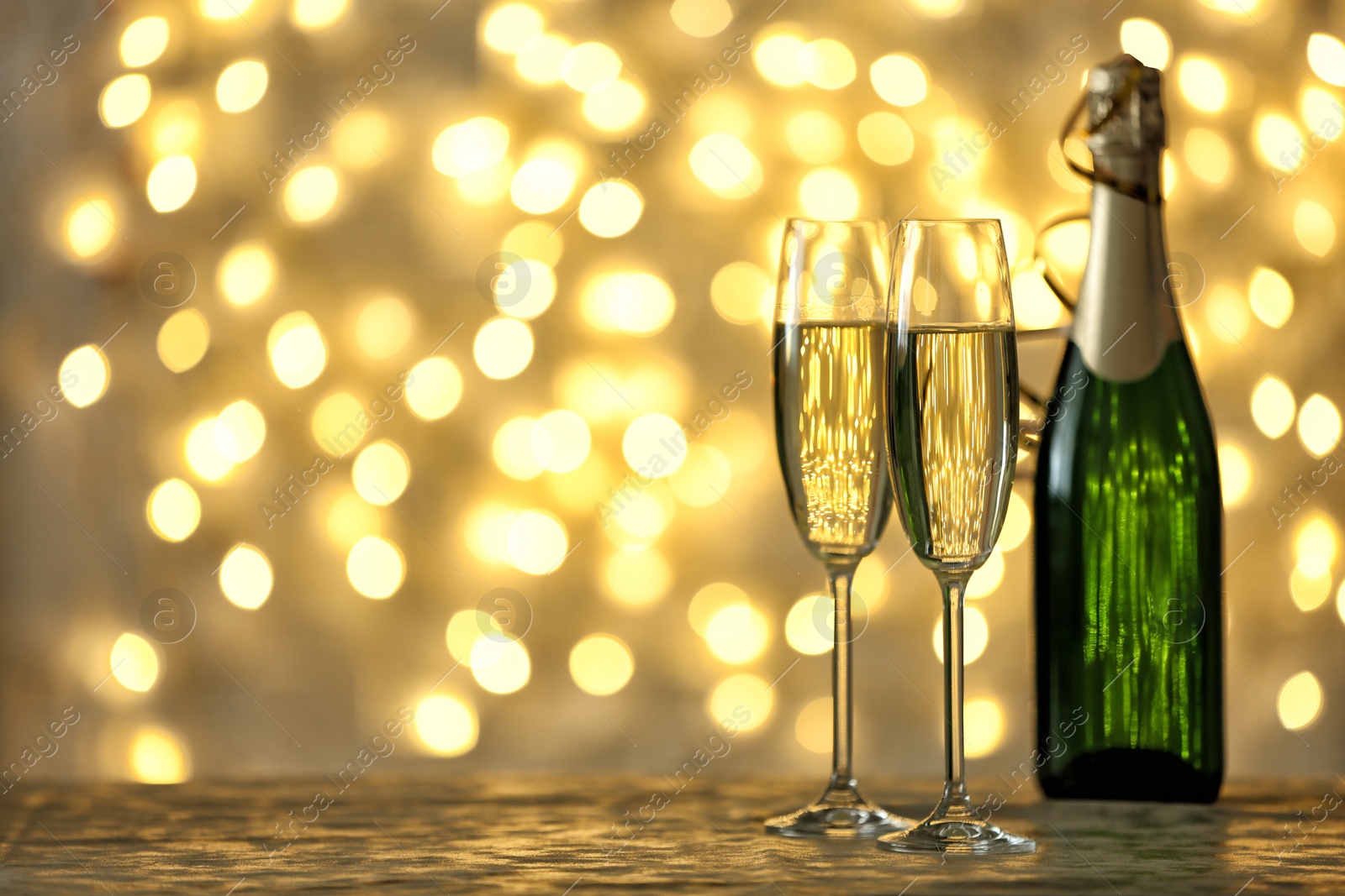 Photo of Glasses and bottle of champagne on table against blurred lights. Space for text