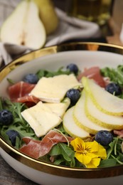Photo of Tasty salad with brie cheese, prosciutto, blueberries and pear in bowl, closeup