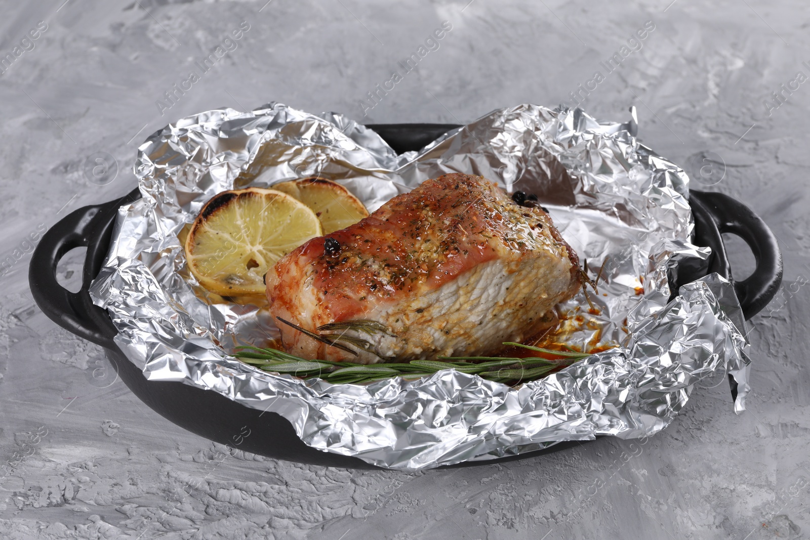 Photo of Tasty pork baked in foil, rosemary and lemon slices on grey textured table, closeup