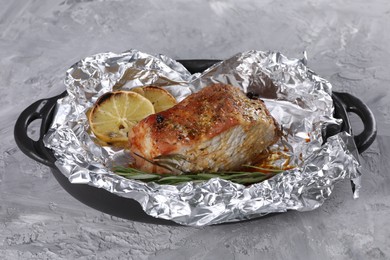 Tasty pork baked in foil, rosemary and lemon slices on grey textured table, closeup