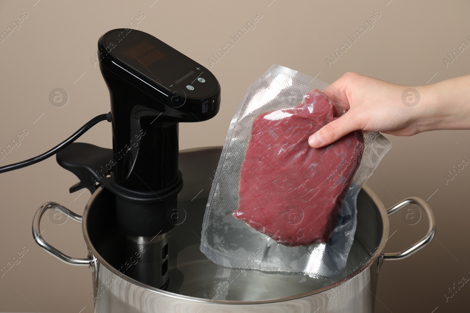 Photo of Woman putting vacuum packed meat into pot with thermal immersion circulator, closeup. Sous vide cooking