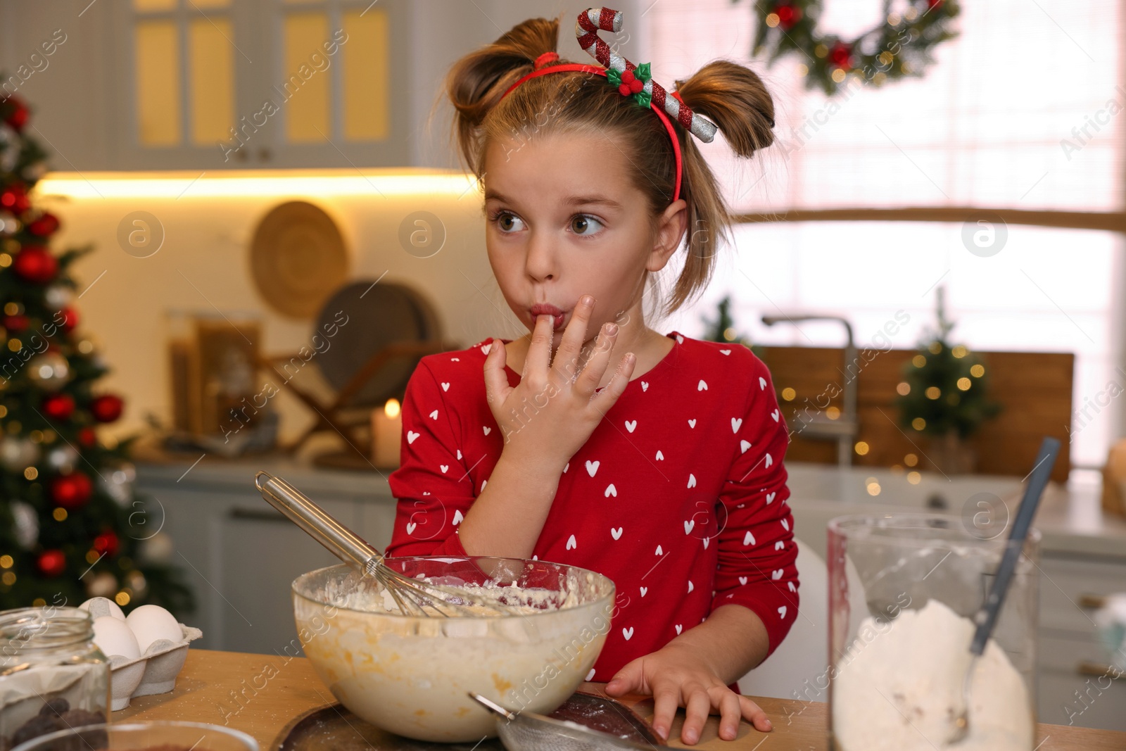 Photo of Cute little girl having fun while making dough for Christmas cookies in kitchen