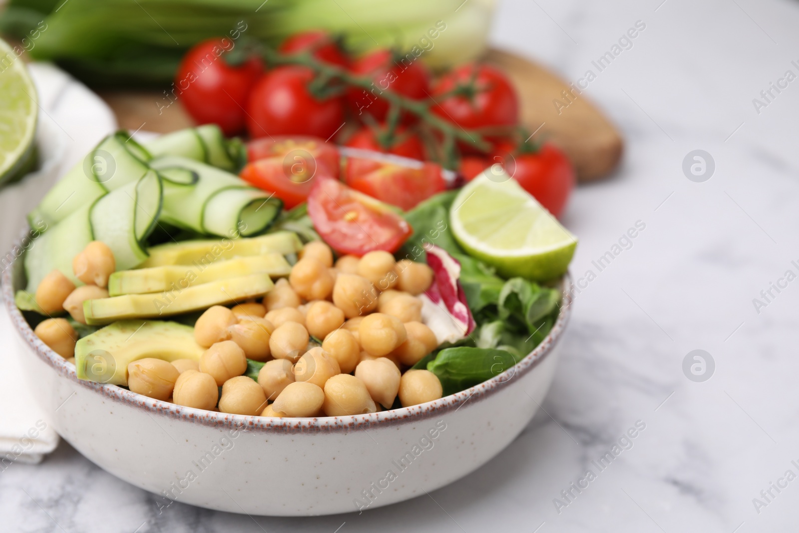 Photo of Tasty salad with chickpeas and vegetables on white marble table, closeup. Space for text