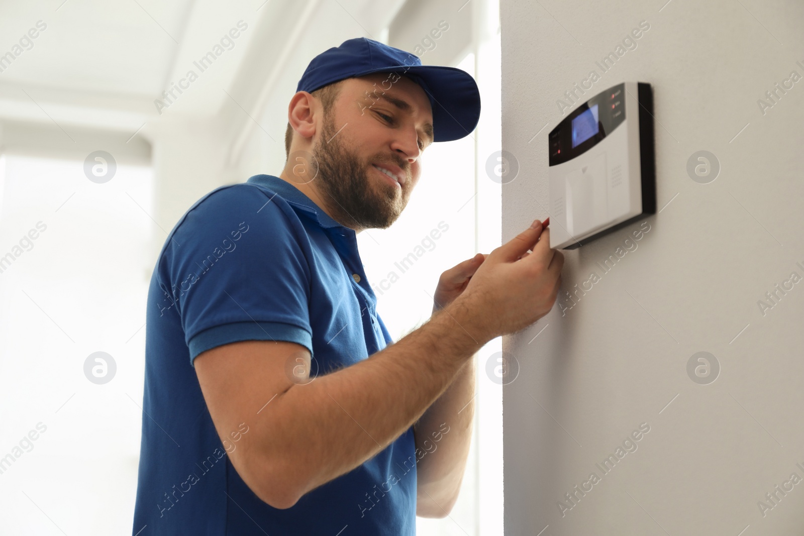 Photo of Man installing home security system on white wall in room