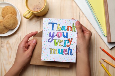 Photo of Woman holding envelope and card with phrase Thank you very much at wooden table, top view