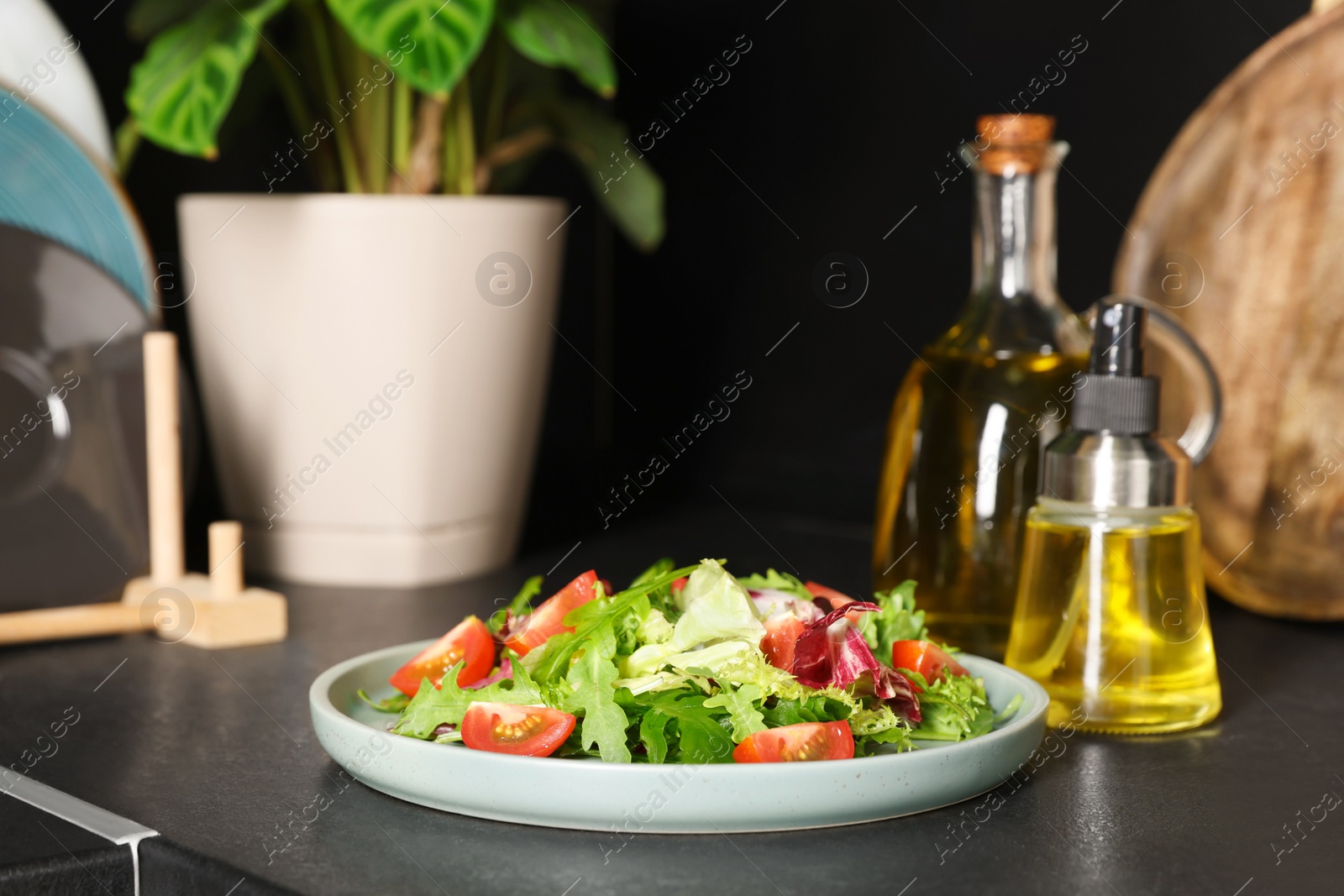 Photo of Plate of salad and bottles with cooking oil on black table in kitchen