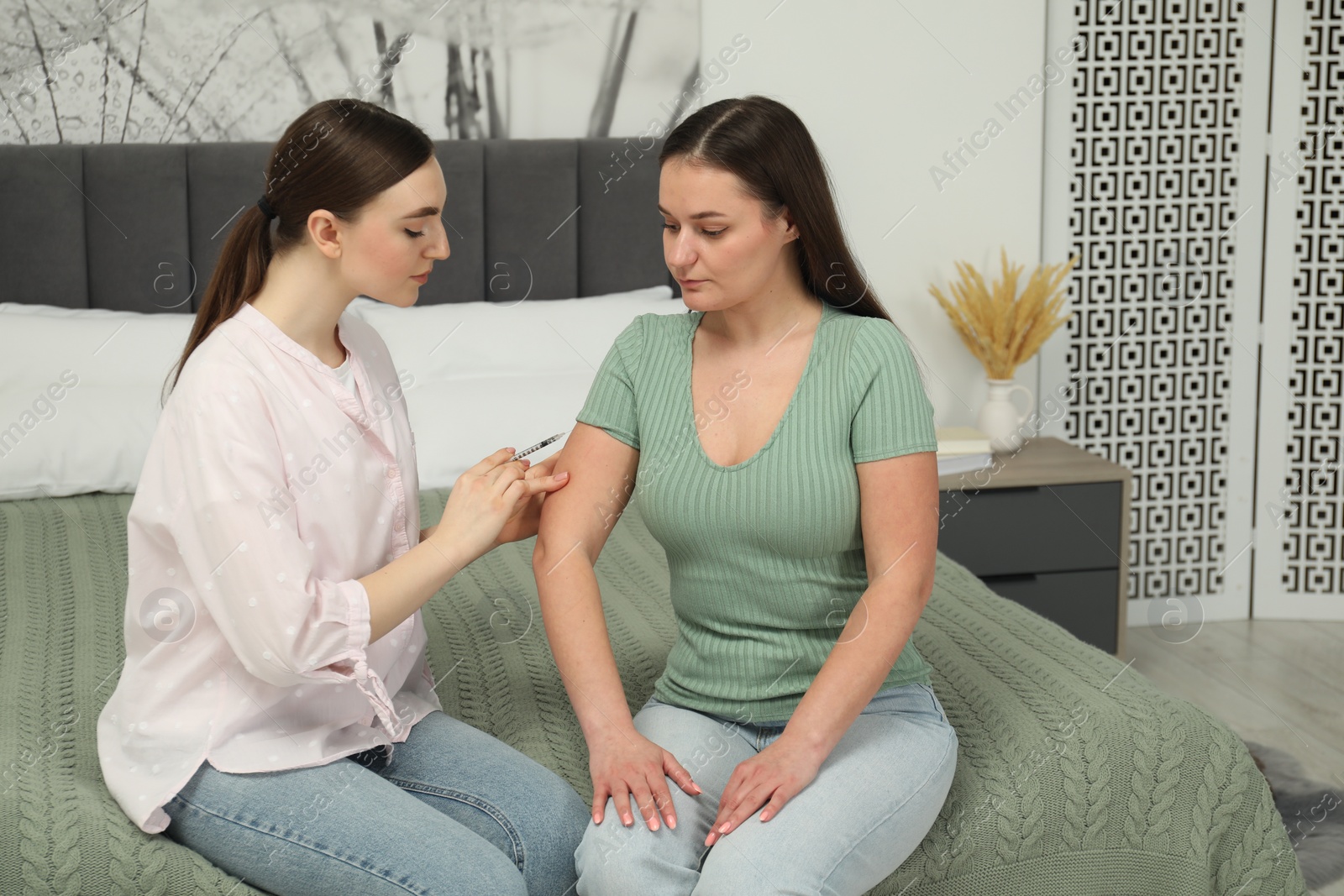 Photo of Woman giving insulin injection to her diabetic friend in bedroom