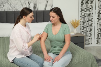 Woman giving insulin injection to her diabetic friend in bedroom