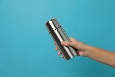 Photo of Woman holding modern thermos on light blue background, closeup