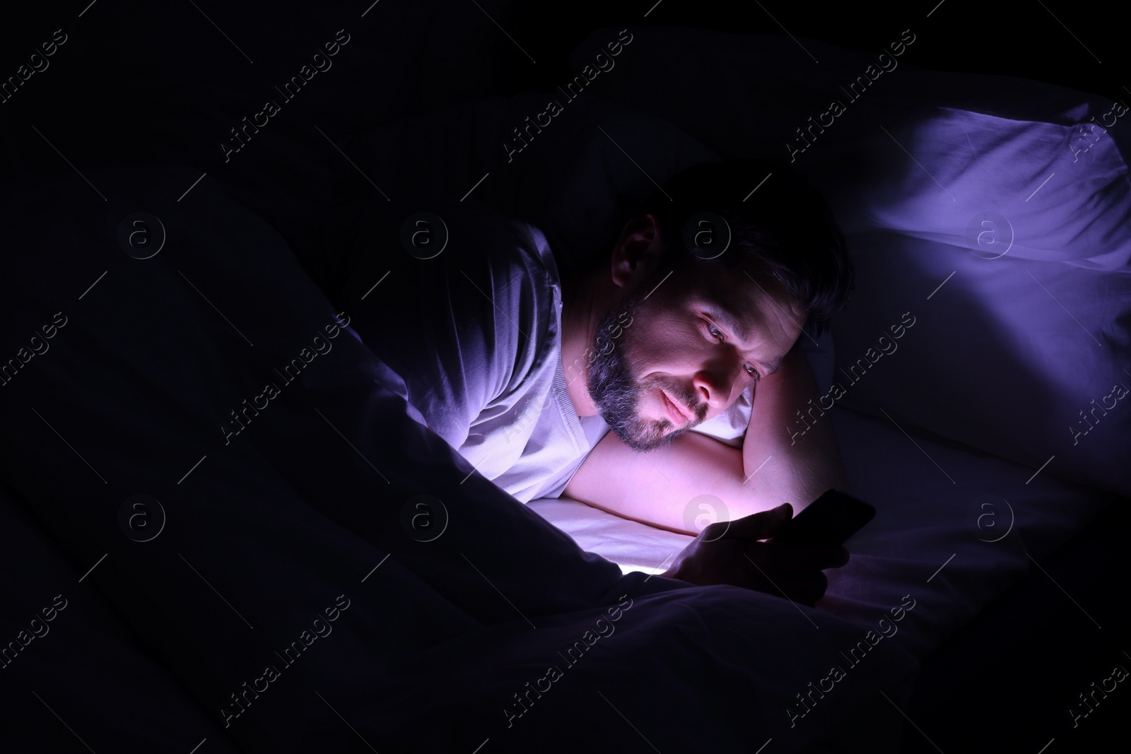 Photo of Man using smartphone in bed at night. Internet addiction