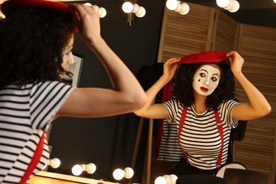 Young woman in mime costume putting beret near mirror indoors