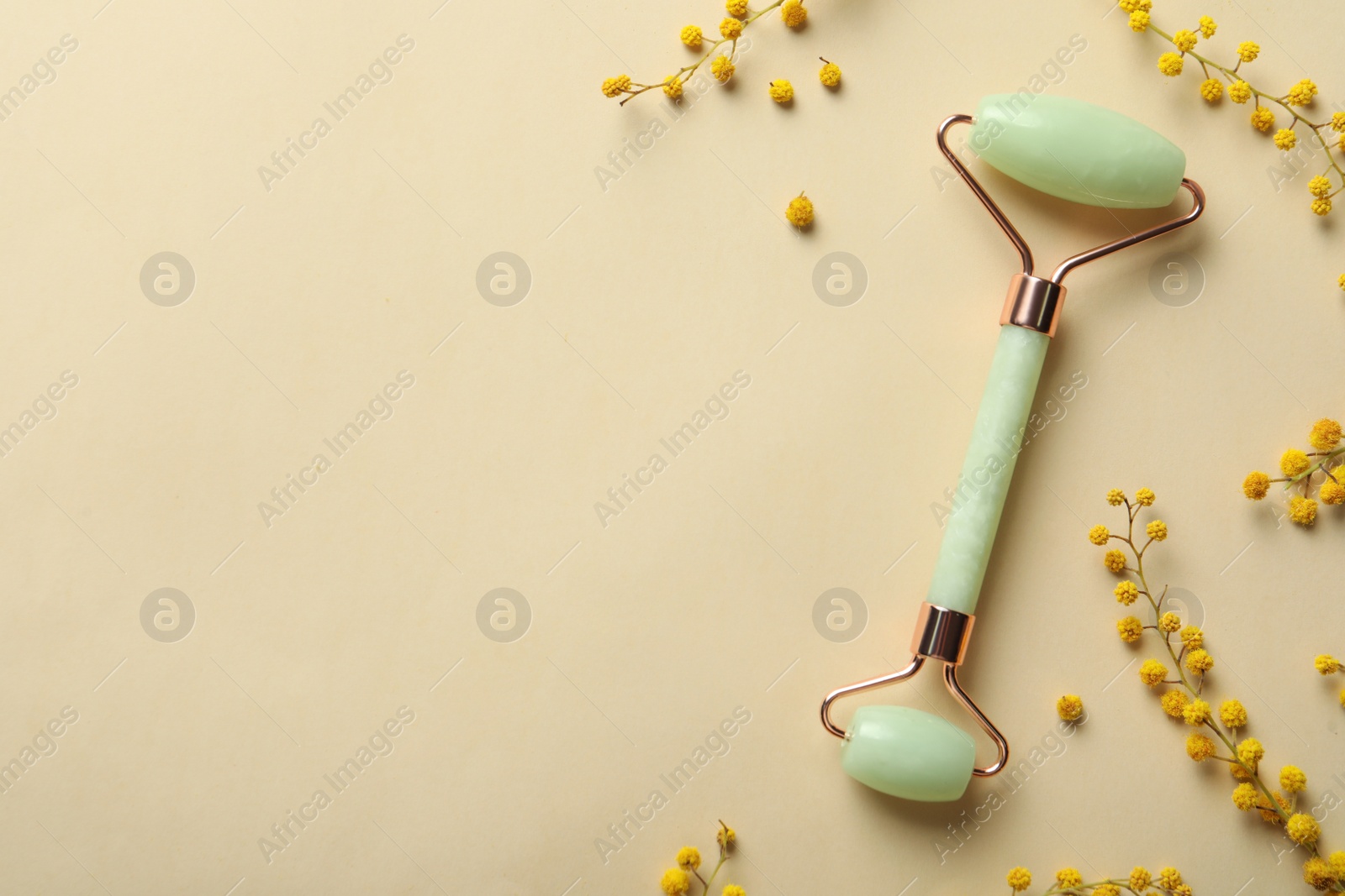 Photo of Natural face roller and flowers on beige background, flat lay. Space for text
