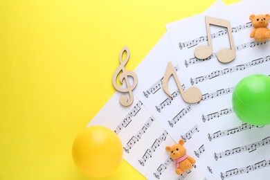 Photo of Baby songs. Music sheets, wooden notes, toy bears and balls on yellow background, top view with space for text