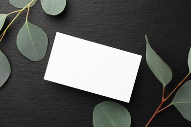 Photo of Blank business card and eucalyptus branches on black background, flat lay. Mockup for design