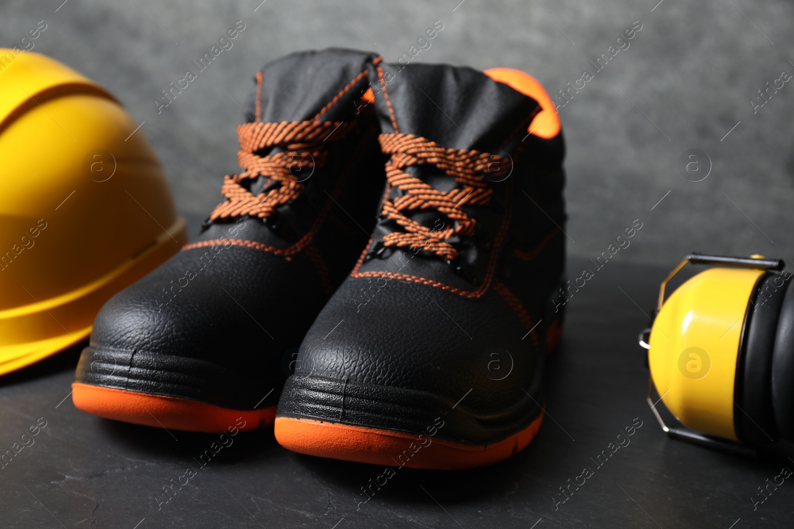 Photo of Pair of working boots, hard hat and earmuffs on gray background, closeup