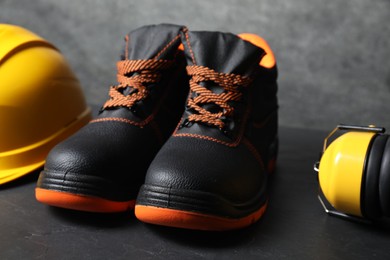 Pair of working boots, hard hat and earmuffs on gray background, closeup