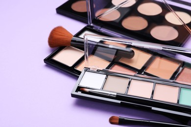 Photo of Colorful contouring palettes with brushes on violet background, closeup. Professional cosmetic product