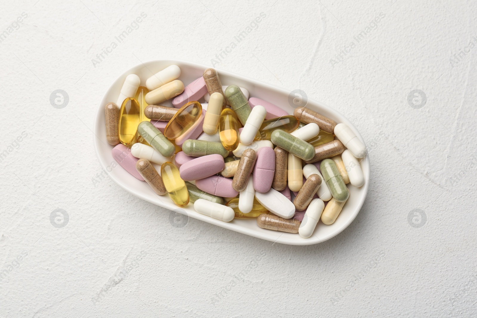 Photo of Different vitamin capsules in bowl on white wooden table, top view