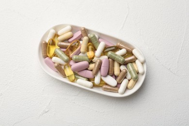 Different vitamin capsules in bowl on white wooden table, top view