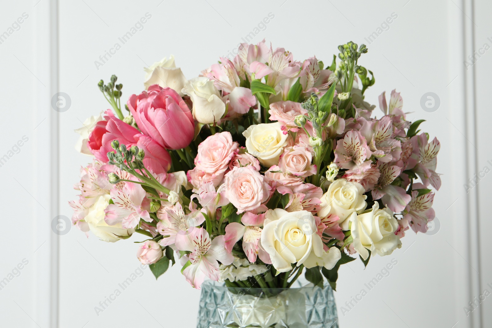 Photo of Beautiful bouquet of fresh flowers in vase near white wall