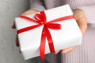 Young woman holding Christmas gift on light background, closeup