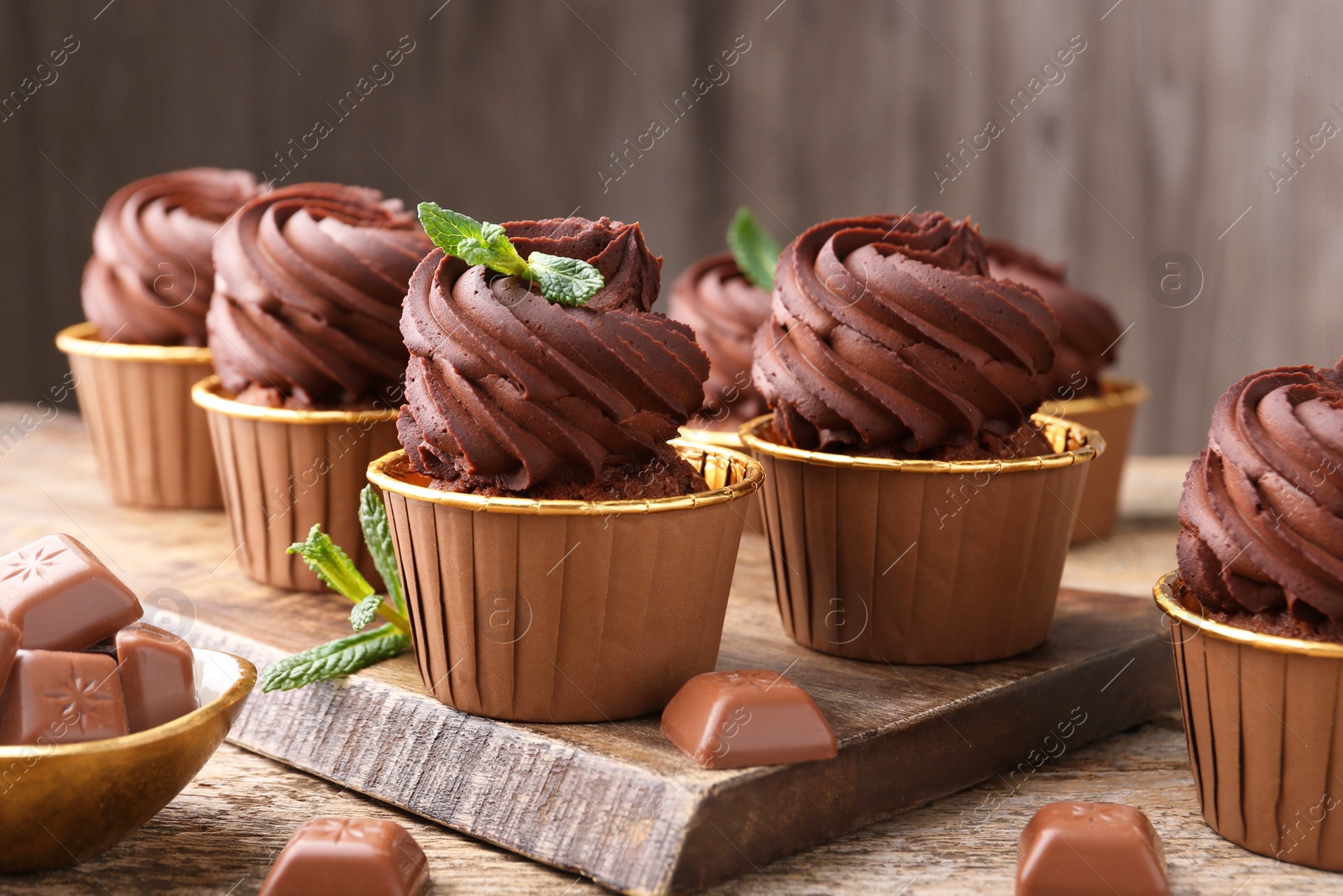 Photo of Delicious cupcakes with chocolate pieces and mint on wooden table