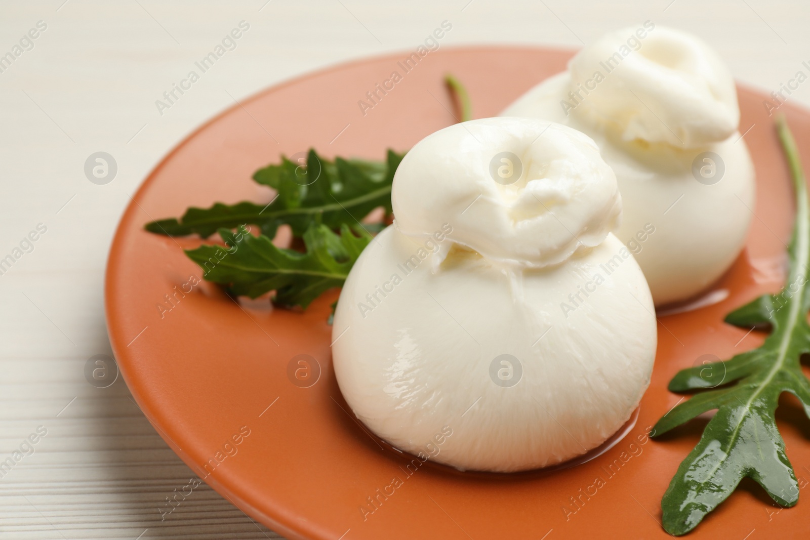 Photo of Delicious burrata cheese with arugula on white wooden table, closeup