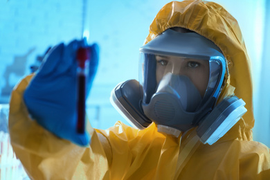 Scientist in chemical protective suit holding test tube with blood sample at laboratory. Virus research