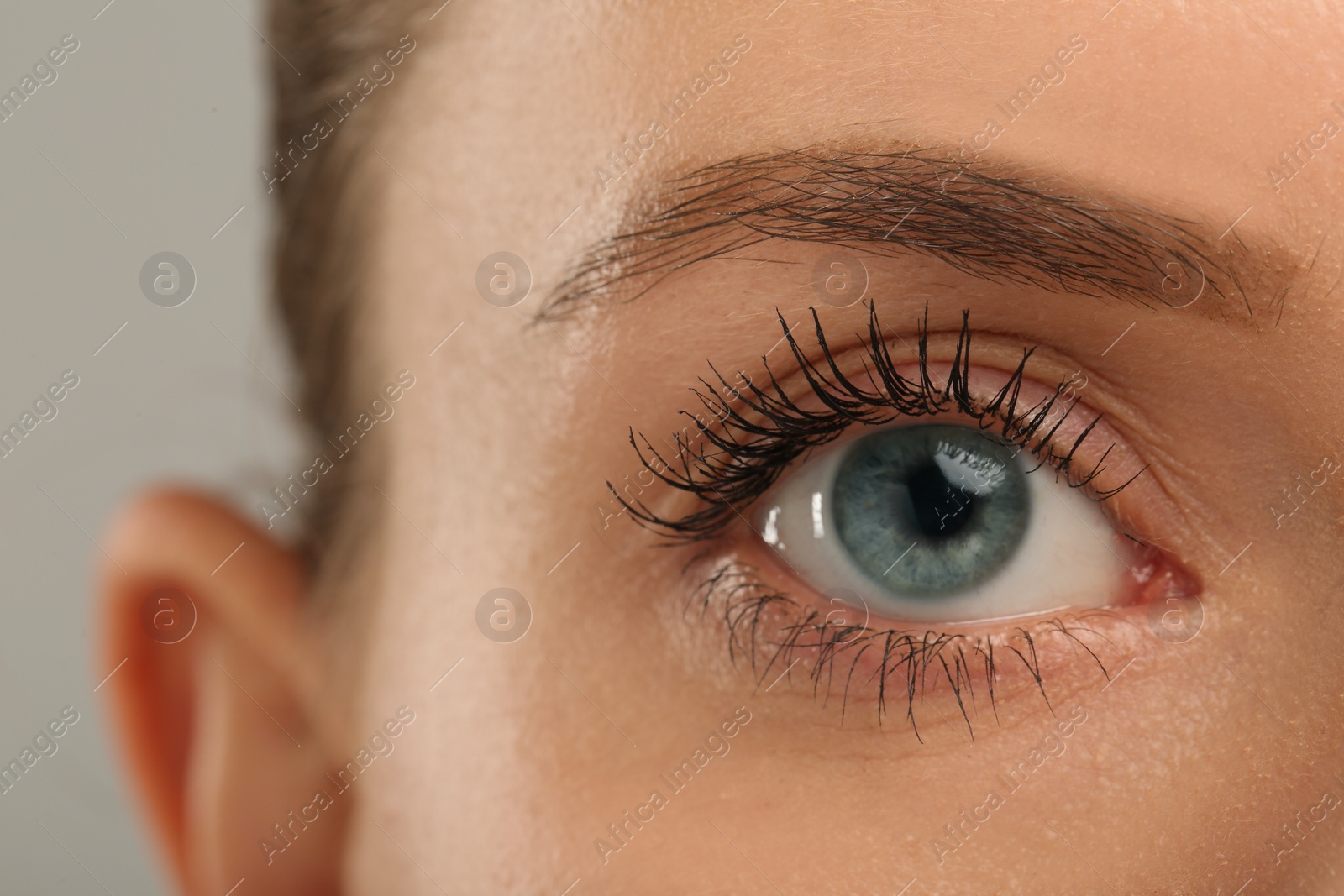 Photo of Woman with long eyelashes after mascara applying against grey background, closeup