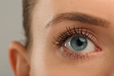 Woman with long eyelashes after mascara applying against grey background, closeup