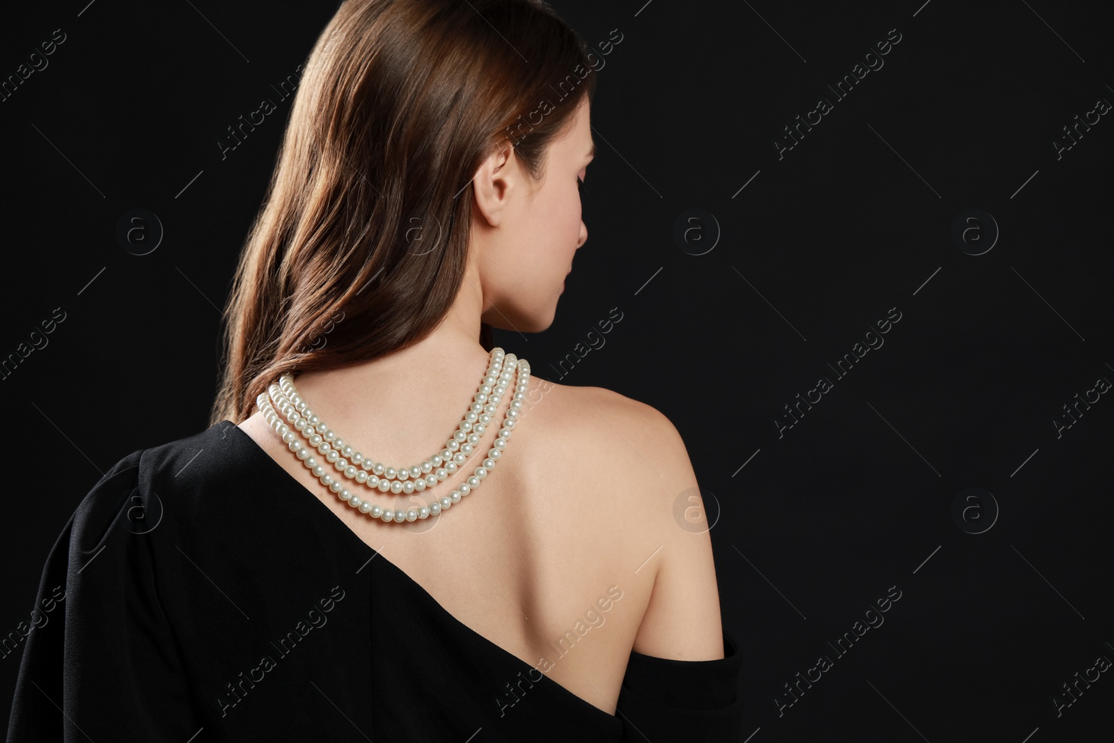 Photo of Young woman wearing elegant pearl necklace on black background, back view. Space for text