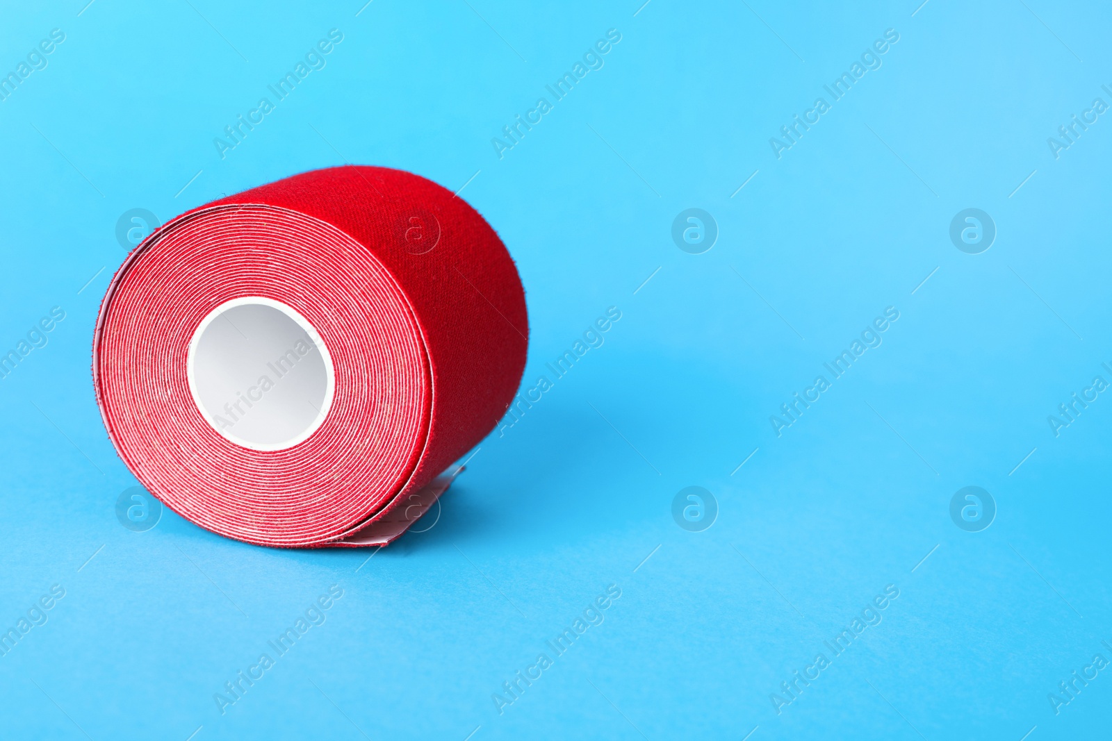Photo of Red kinesio tape in roll on light blue background. Space for text