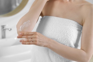 Photo of Woman applying body cream onto elbow in bathroom, closeup