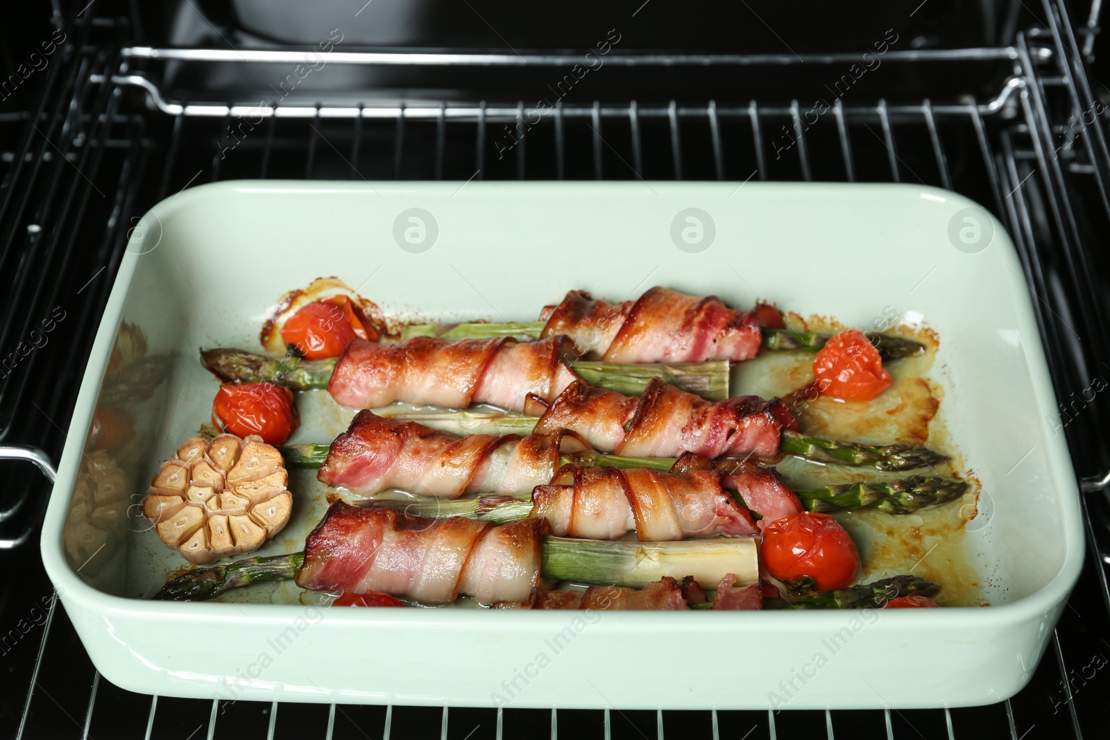 Photo of Bacon wrapped asparagus in baking dish on oven rack, closeup