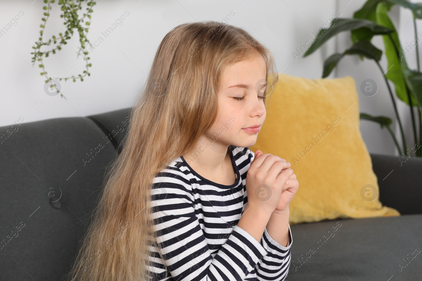 Photo of Girl with clasped hands praying on sofa at home