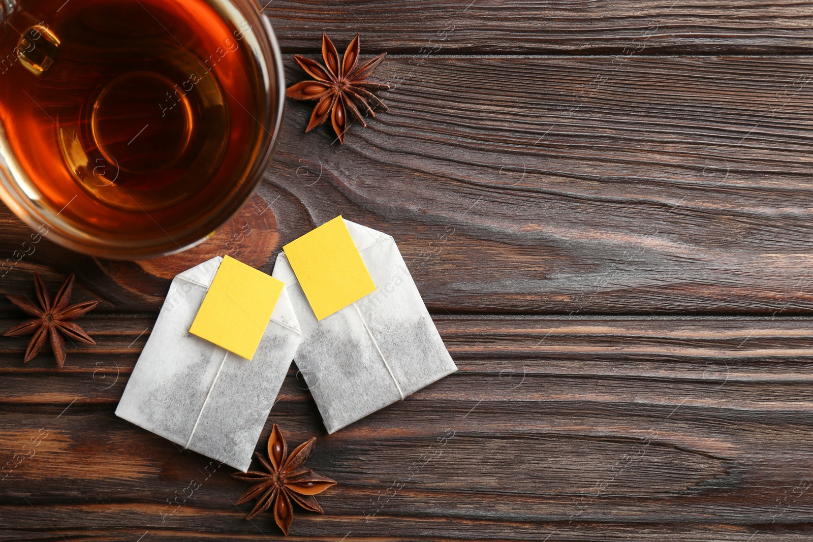 Photo of Tea bags, cup of hot drink and anise stars on wooden table, flat lay. Space for text