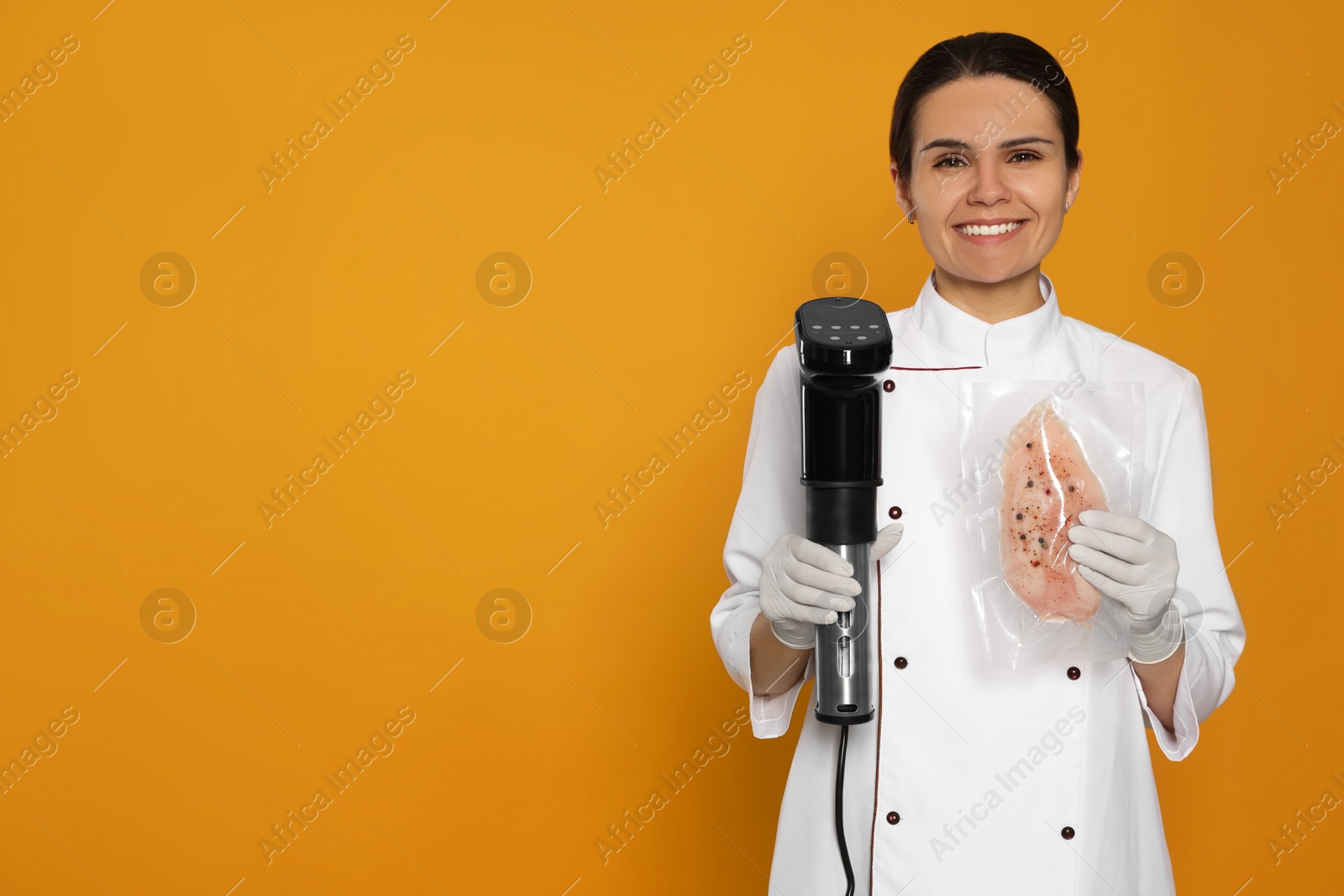 Photo of Chef holding sous vide cooker and meat in vacuum pack on orange background. Space for text