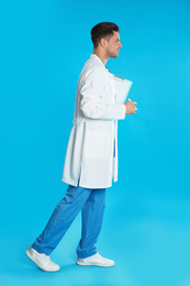 Photo of Doctor in uniform with clipboard walking on blue background