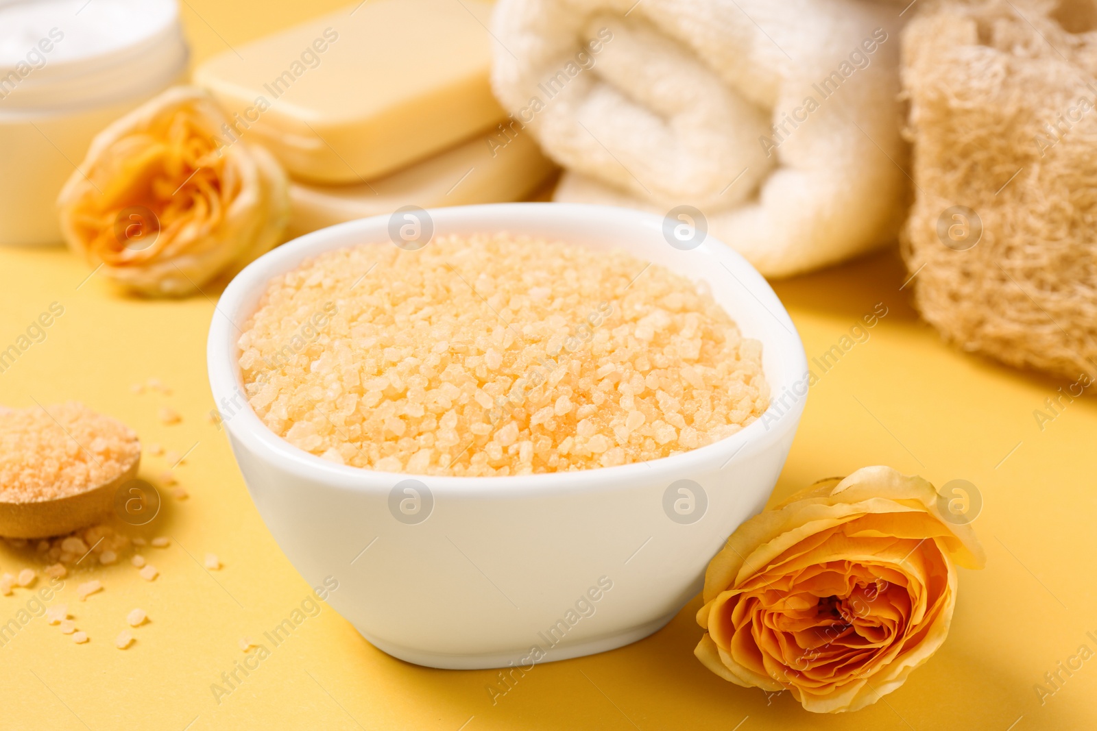 Photo of Bowl with sea salt, soap bars and beautiful roses on yellow background, closeup