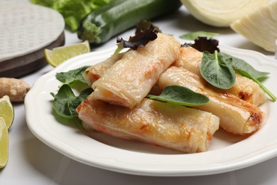 Photo of Plate with tasty fried spring rolls and spinach on white tiled table, closeup