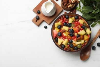 Delicious fruit salad in bowl, berries, fresh mint and nuts on white marble table, flat lay. Space for text