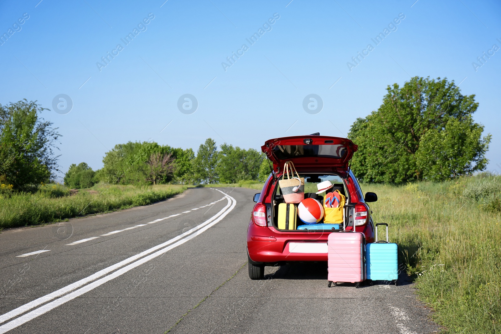 Photo of Suitcases near family car with open trunk full of luggage on highway. Space for text