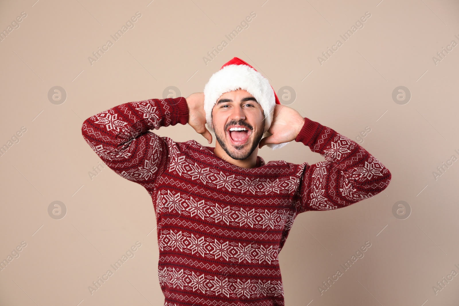 Photo of Portrait of young man in Christmas sweater and Santa hat on beige background