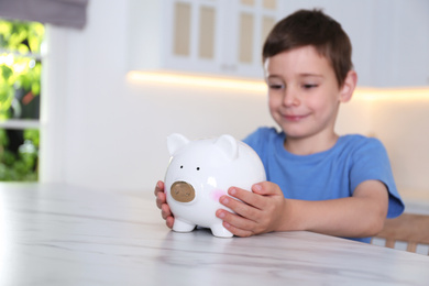 Little boy with piggy bank at marble table indoors