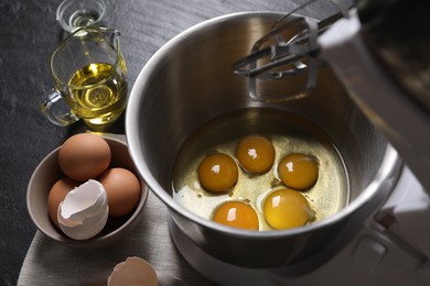 Making dough. Raw eggs in bowl of stand mixer and ingredients on black table, closeup