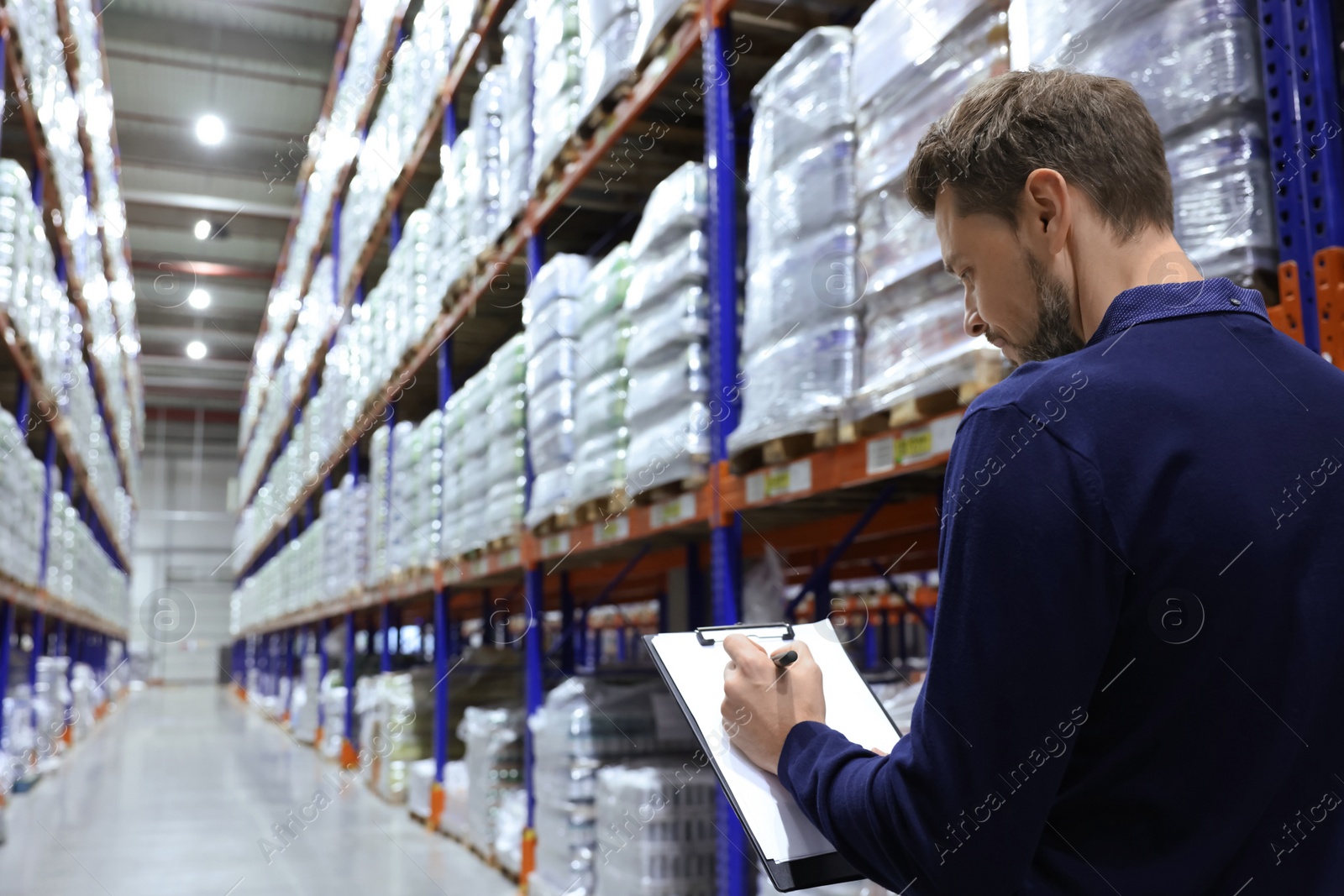 Photo of Manager holding clipboard in warehouse with lots of products, back view. Space for text