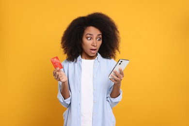 Photo of Shocked woman with credit card and smartphone on orange background. Debt problem