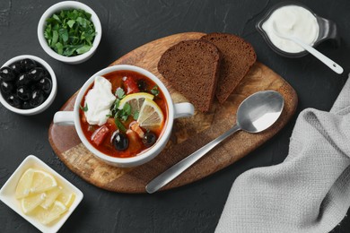 Photo of Meat solyanka soup with sausages, olives and vegetables served on dark grey textured table, flat lay